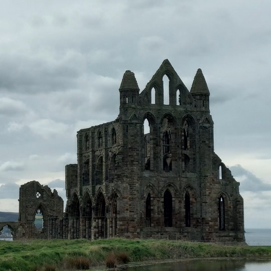 a stone building with a body of water in the background with Whitby Abbey in the background