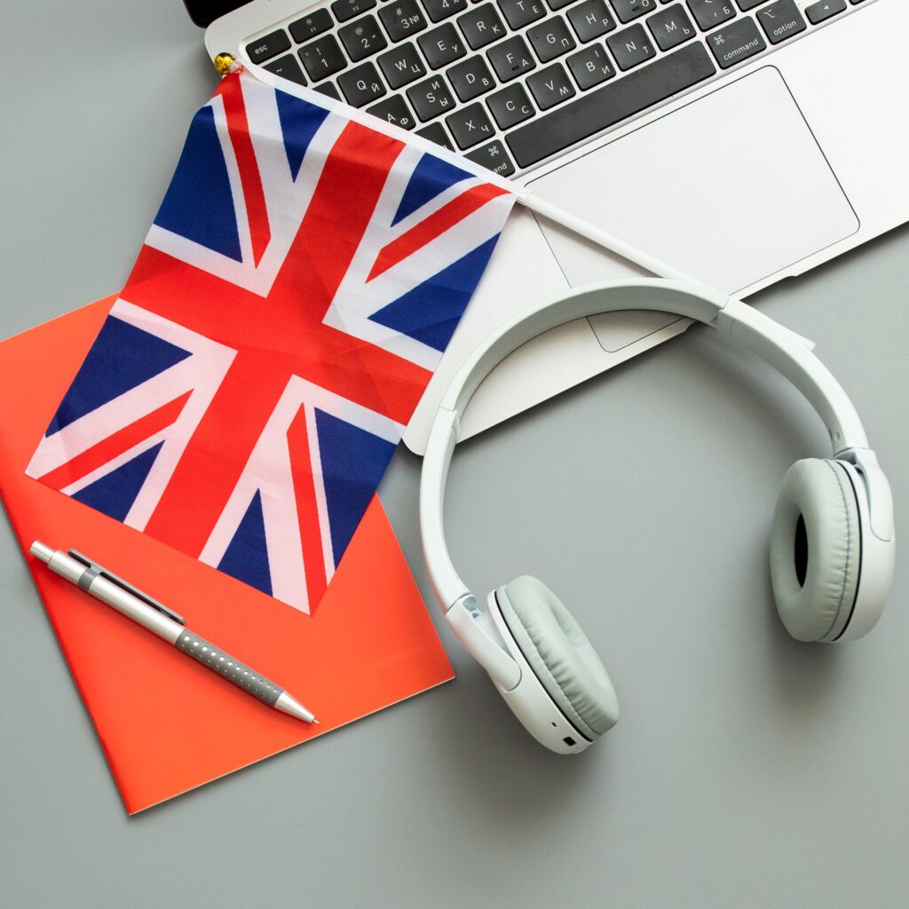 A pair of headphones with a Union Jack flag, on top of a notepad with a pen at the side.